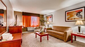 A hotel room with a sofa, a coffee table, a desk, a lamp, and a large window with orange curtains.