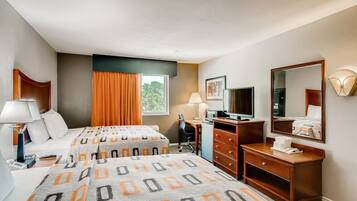 Una habitación de hotel con una cama, un escritorio con computadora, un aparador, un espejo y una ventana con cortinas.
