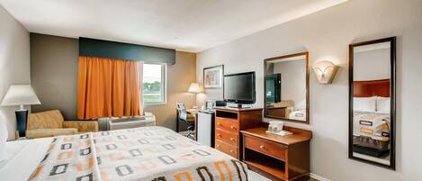 A hotel room with a bed, desk, television, dresser, and a large mirror.