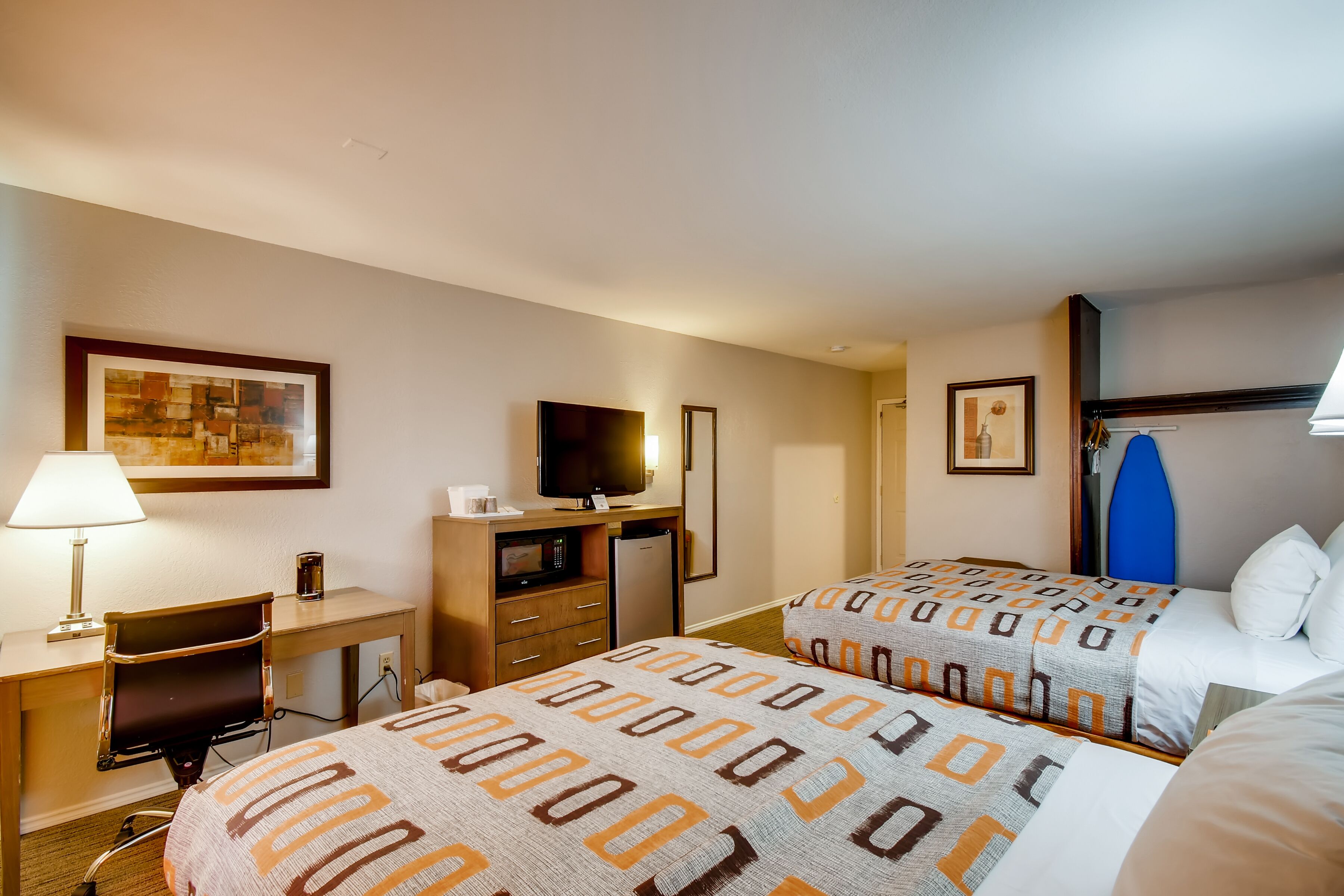 A hotel room with two beds, a desk with a chair, a television, a refrigerator, and a microwave.