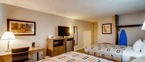 Habitación de hotel con dos camas, un escritorio con silla, televisión, refrigerador y microondas.