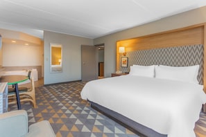 Habitación de hotel con una cama grande, un escritorio con silla, una mesita de noche con lámpara y un piso estampado.