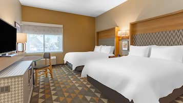 A hotel room with two beds, a desk with a TV, and a patterned carpet.