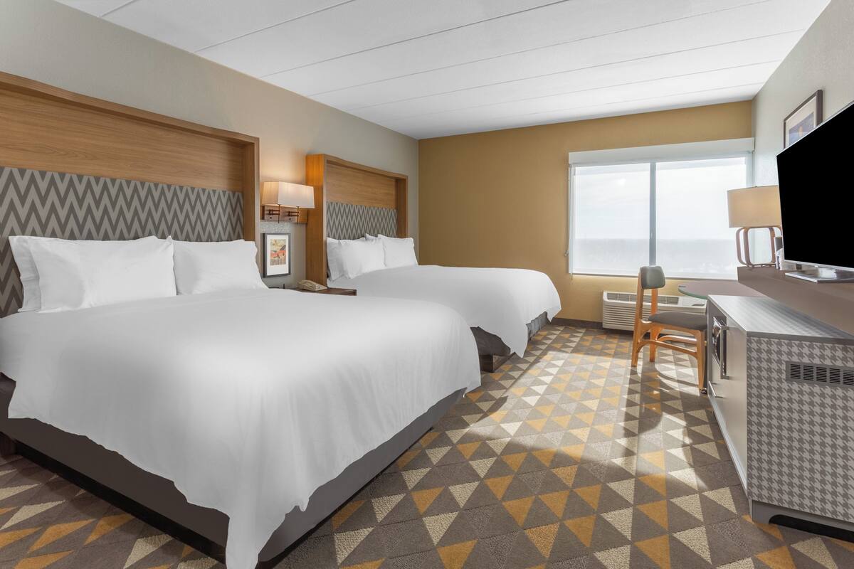 A hotel room with two beds, a desk, a TV, and a large window.