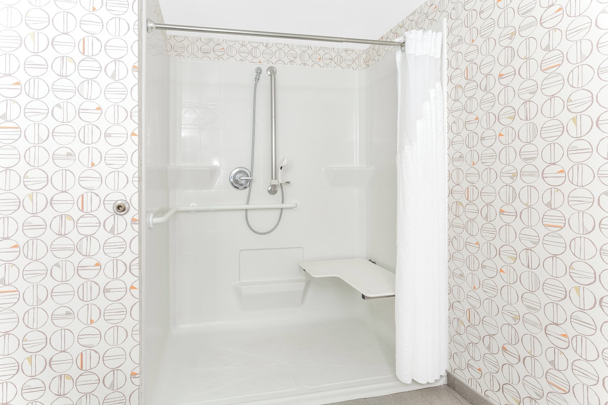 Una ducha con cabezal de ducha de mano, cabezal de ducha de mano y asiento para ducha.
