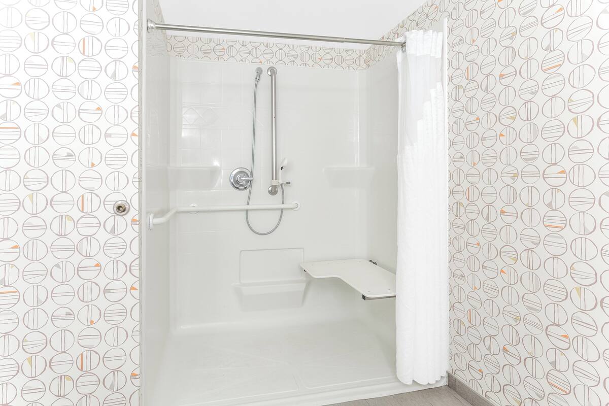 A shower with a handheld showerhead, a handheld showerhead, and a shower seat.