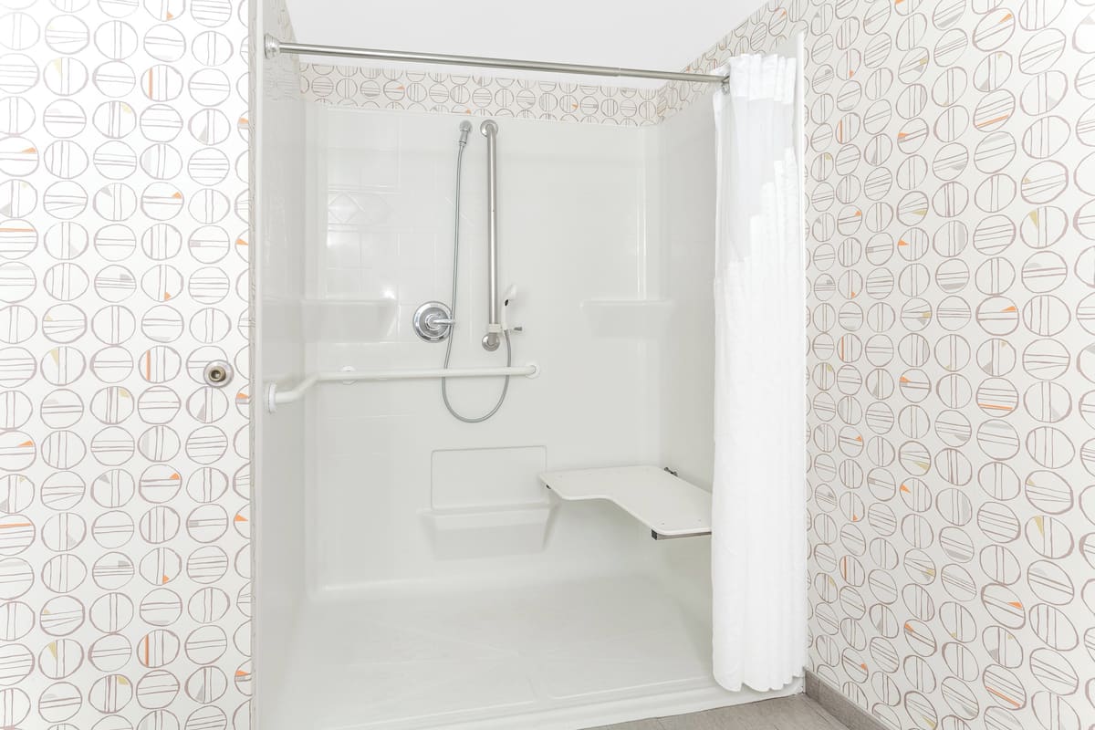 A shower with a handheld showerhead, a handheld showerhead, and a shower seat.
