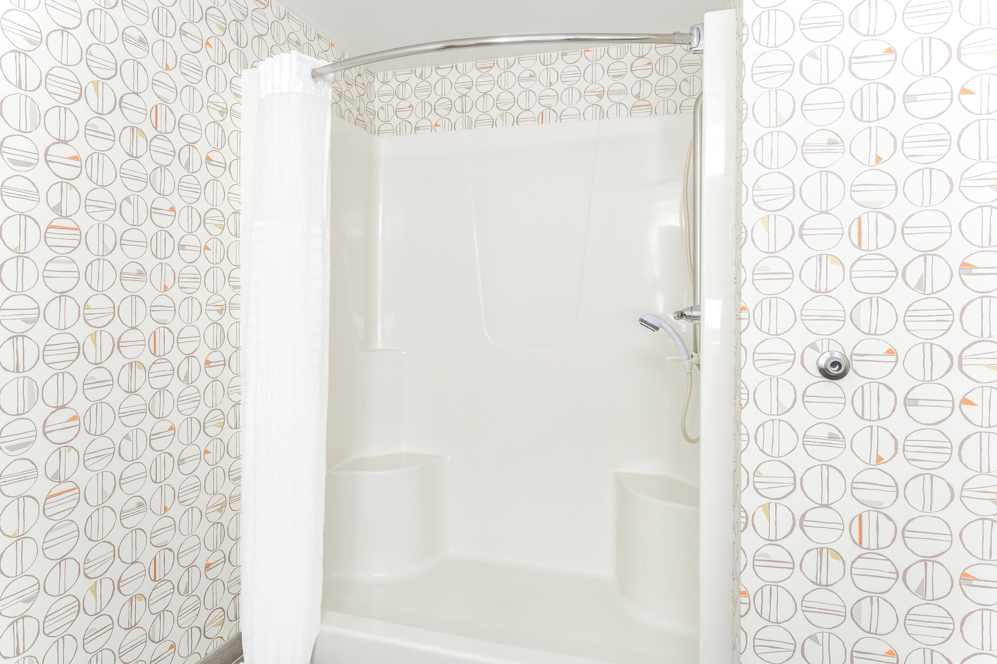 A shower with a white curtain, a showerhead, and a wall with a circular pattern.