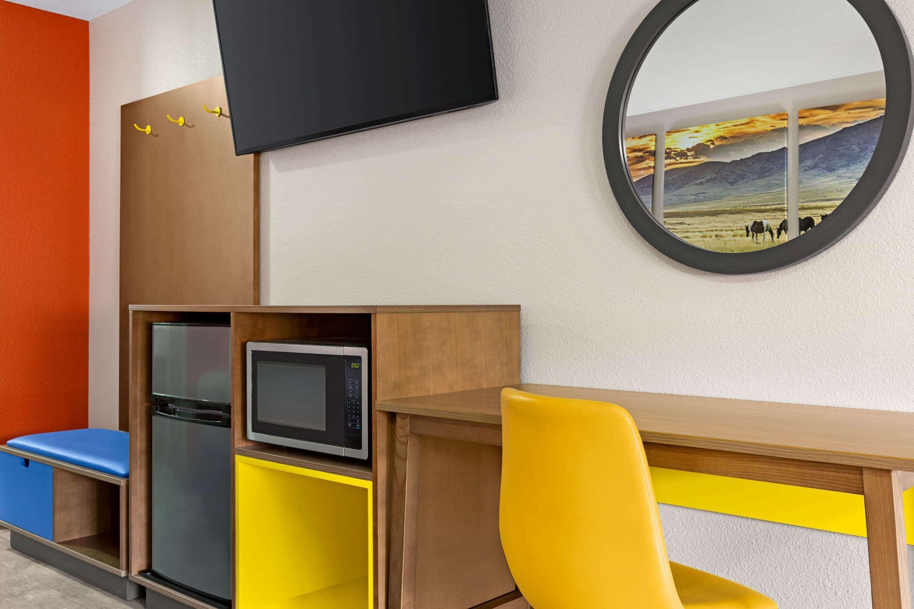 Una habitación moderna con un escritorio de madera, una silla amarilla y un televisor de pantalla plana montado en la pared.