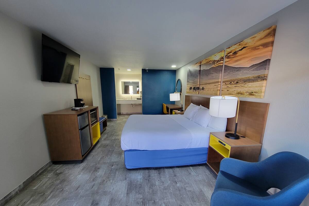 A hotel room with a bed, bedside tables, a desk, a chair, a mirror, and a painting on the wall.