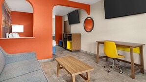 A room with a wooden desk, a yellow chair, a grey sofa, and a TV mounted on the wall. - Days Inn by Wyndham Ruidoso Downs (Ruidoso Downs)