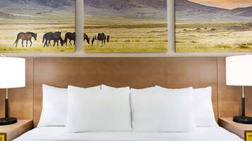 Une chambre d’hôtel avec un lit, deux tables de chevet avec des lampes et un grand tableau représentant un paysage, placé au-dessus du lit.