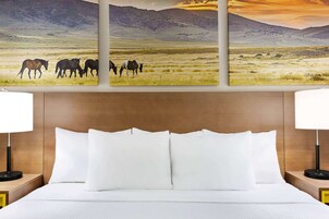 A hotel room with a bed, two bedside tables with lamps, and a large landscape painting above the bed.