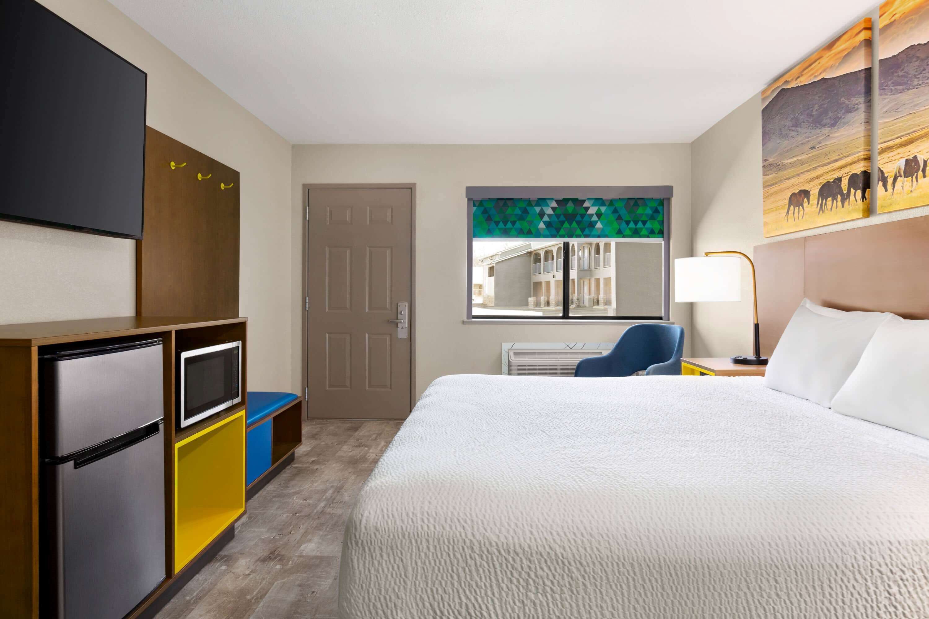 Une chambre d’hôtel avec un lit, un bureau et une chaise, une télévision et un tableau accroché au mur.
