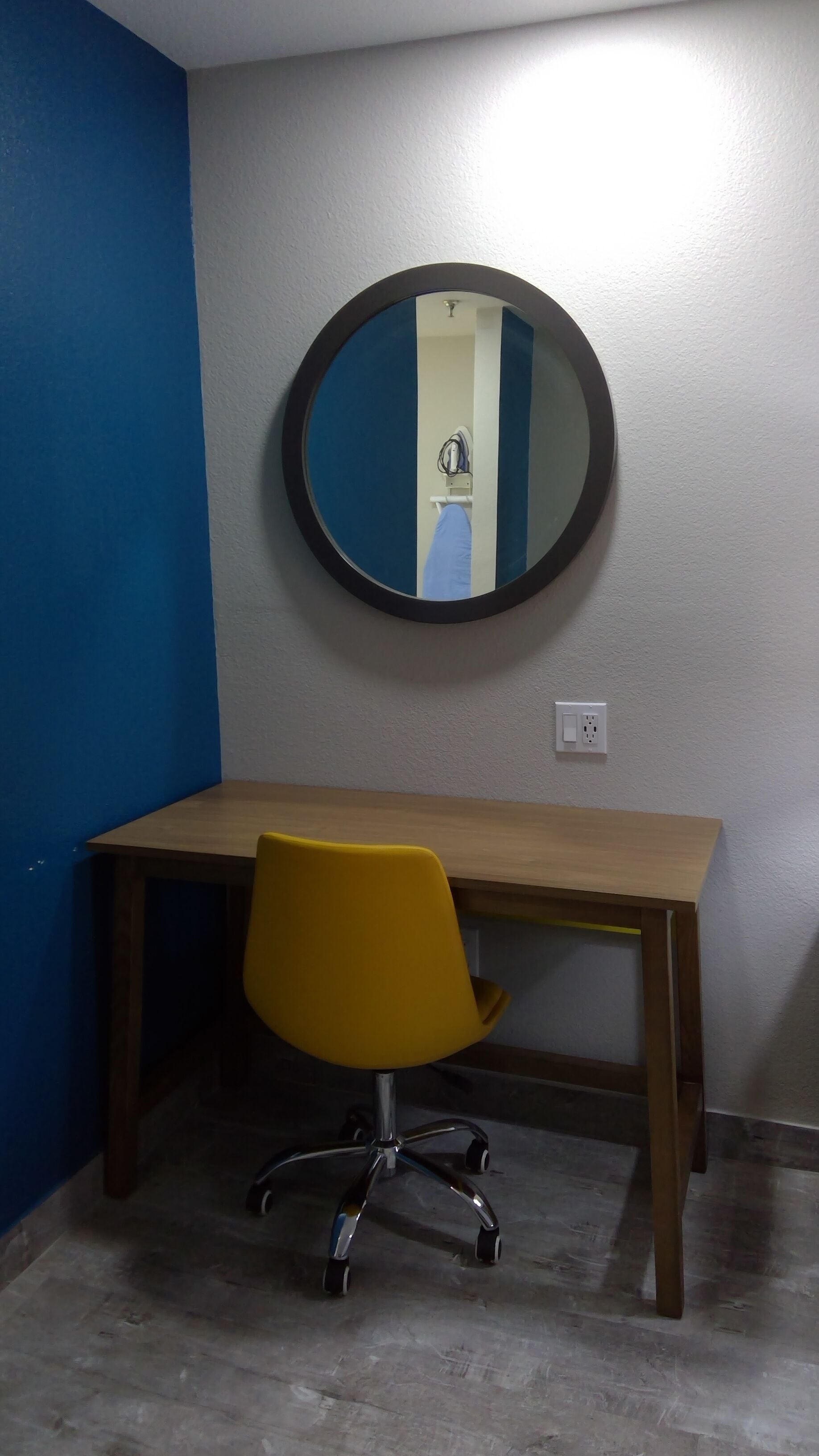 Una habitación con un escritorio de madera, una silla de oficina amarilla y un espejo redondo en la pared.