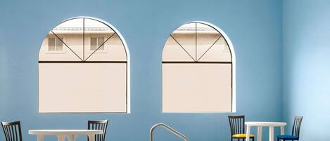 A room with two arched windows, a pool, and two tables with chairs.