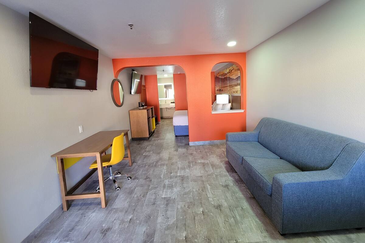 A room with a blue sofa, a wooden desk with a yellow chair, an orange accent wall, and a mirror.