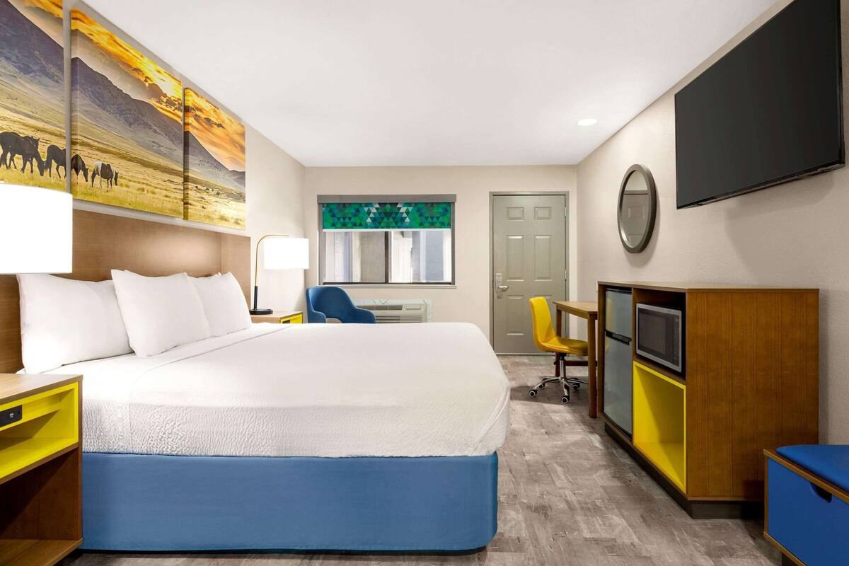 A hotel room with a large bed, a desk, a TV, and a painting on the wall.