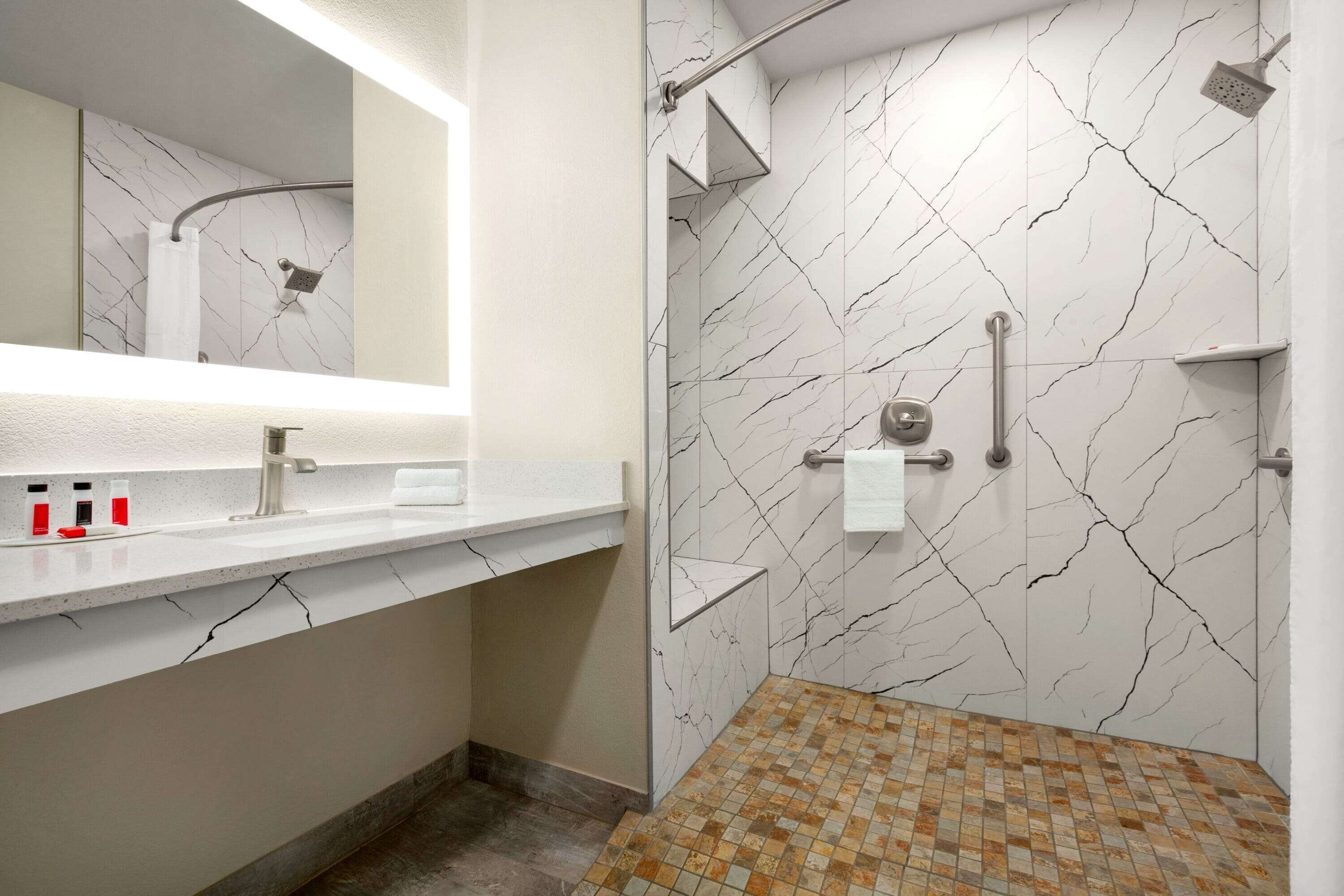 Uma casa de banho moderna com painel de salpicão de mármore branco, chuveiro com chuveiro manual, lavatório com torneira e chão em mosaico.