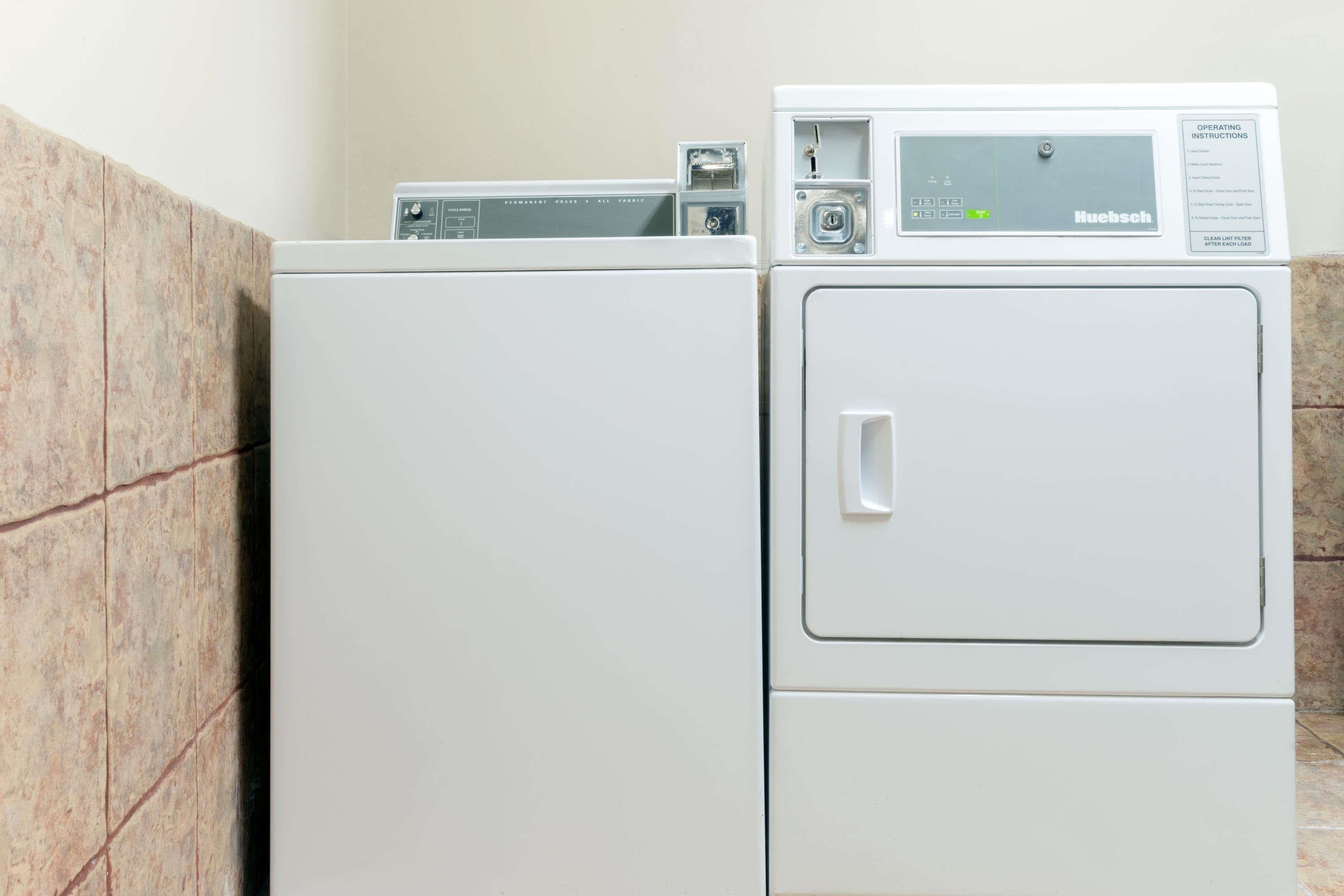 A front-loading white Huebsch washer and dryer stacked in a laundry room with a tiled wall.
