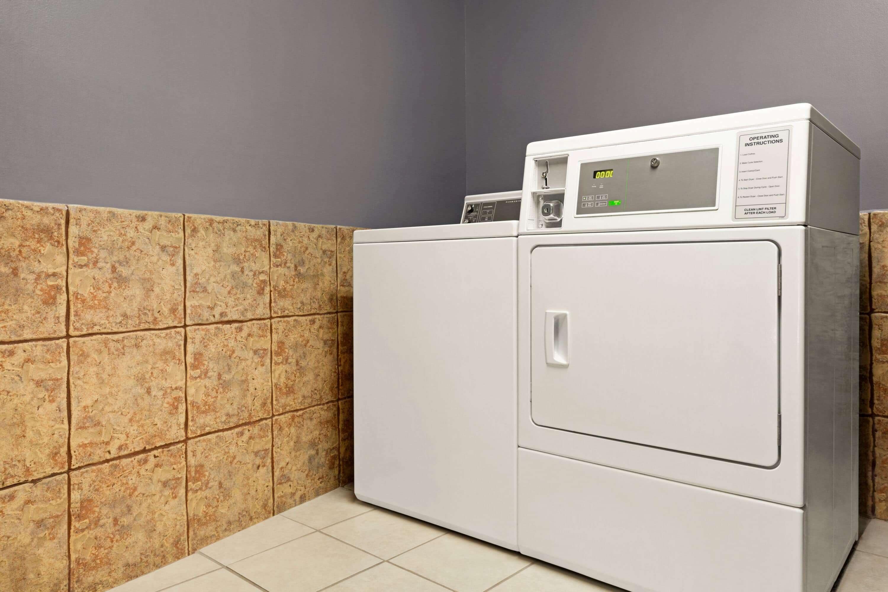 A front-loading washing machine in a laundry room with tiled walls and floor.