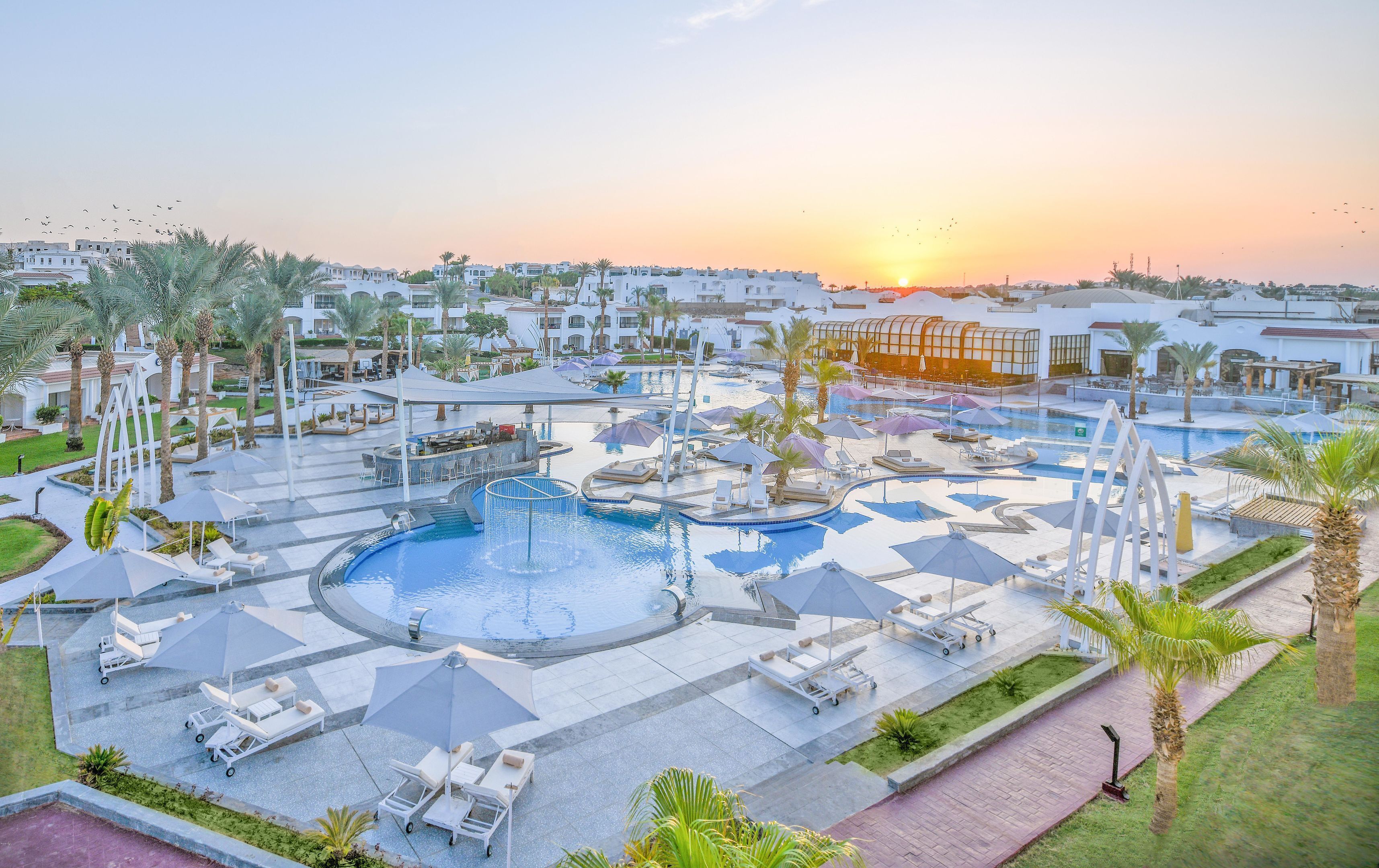A resort with multiple swimming pools, lounge chairs, and palm trees.