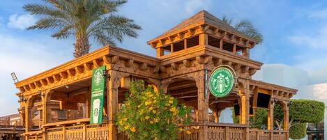 Un bâtiment en bois orné du logo de Starbucks, une enseigne indiquant la présence d’un restaurant, et un palmier en arrière-plan.