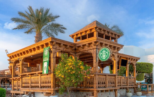 A wooden building with a Starbucks logo, a sign indicating a restaurant, and a palm tree in the background.