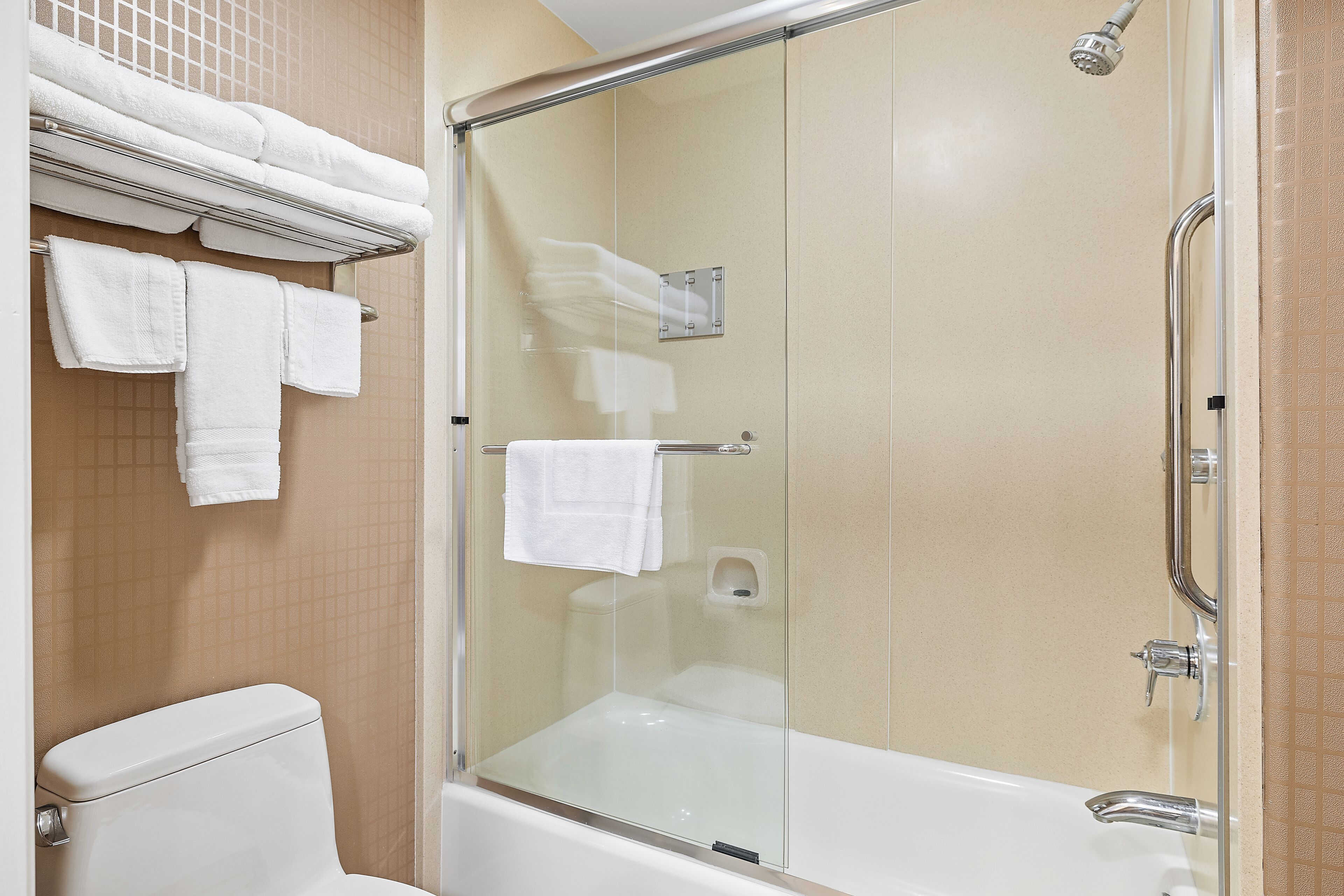A modern bathroom with a glass-enclosed shower, a white bathtub, and neatly arranged white towels on a rack.