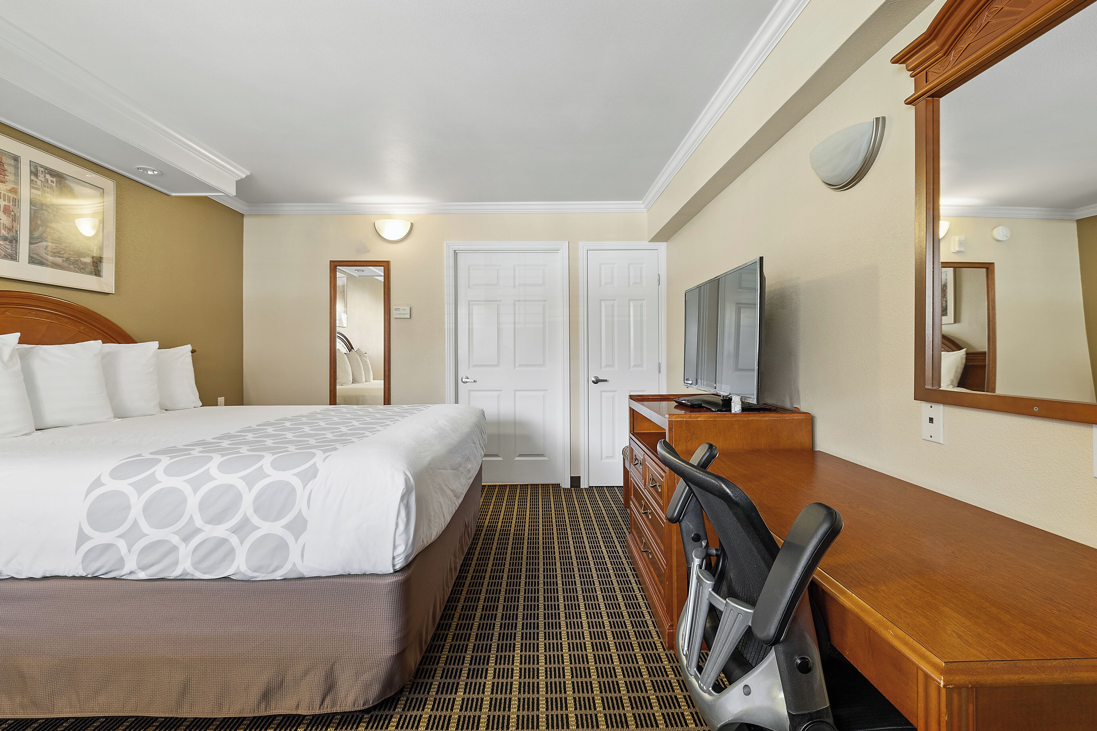 Een hotelkamer met een bed, een bureau, een stoel, een televisie en een spiegel.