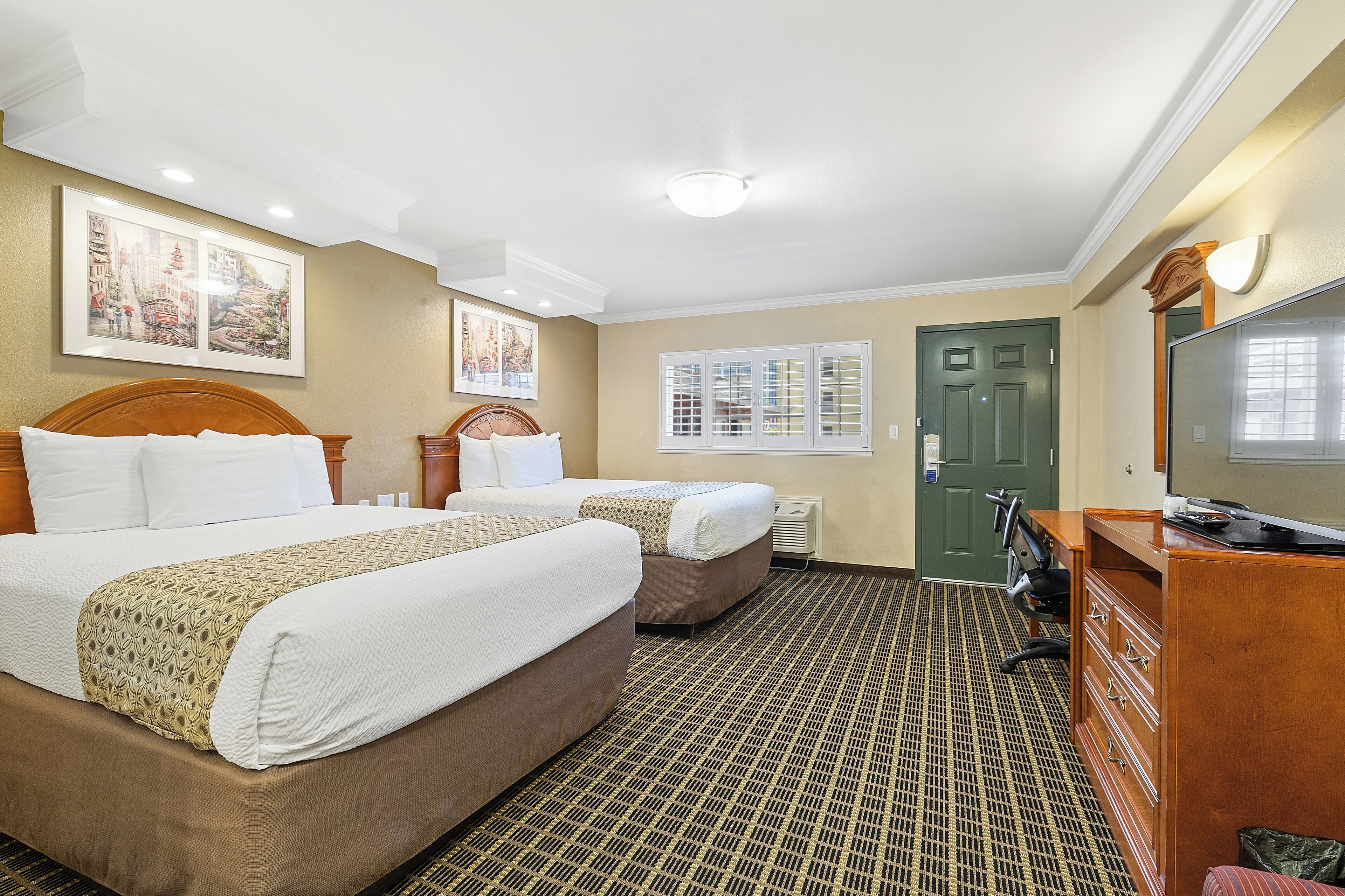 A hotel room with two beds, a dresser, a desk, and a television.
