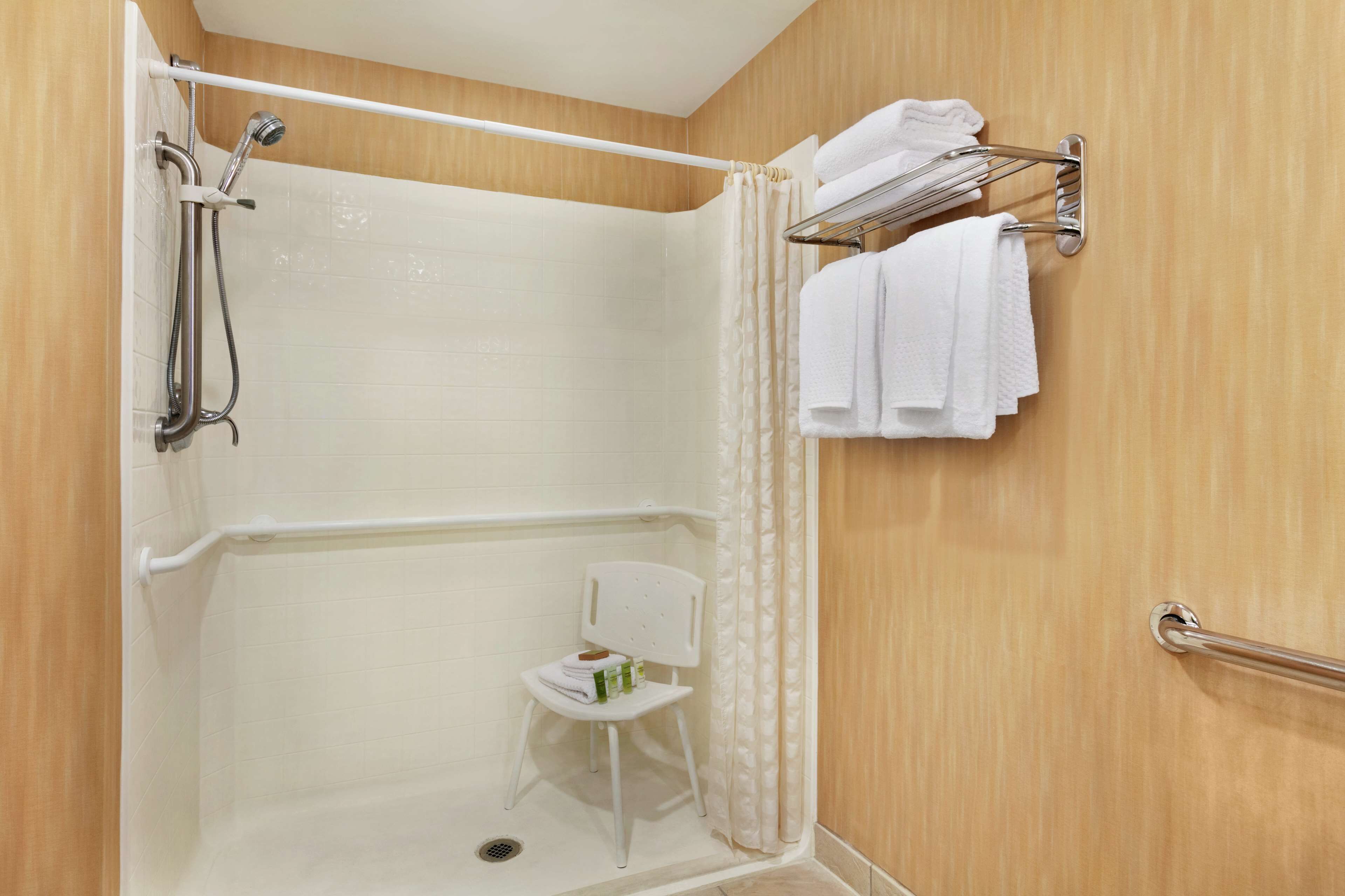 A shower area with a white chair, a towel rack, and a showerhead.