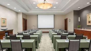 Un salón de conferencias con mesas y sillas, una pantalla de proyector y una lámpara de araña grande.