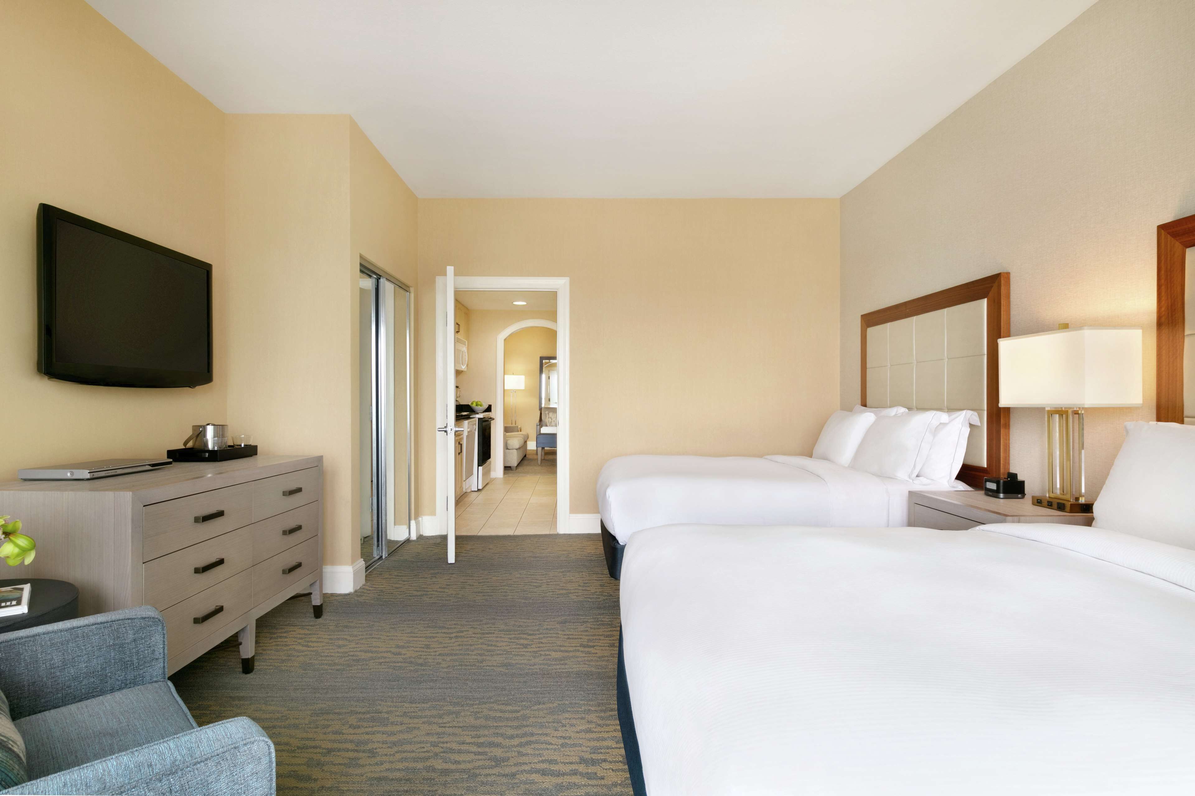 A hotel room with two beds, a desk, a TV, and a bathroom visible through an open door.