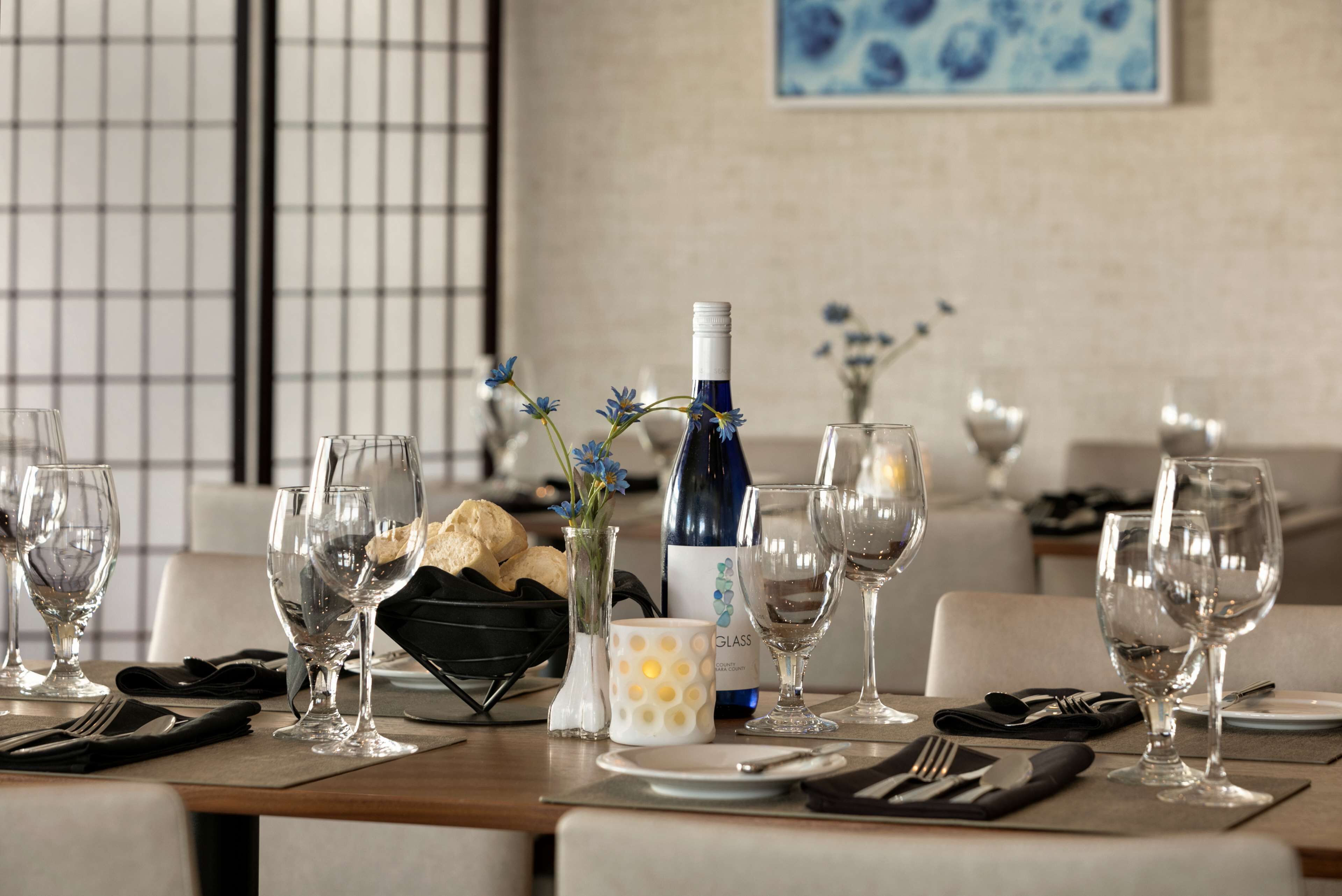 A dining table set with wine glasses, a bottle of wine, a vase with flowers, and a bowl of bread.