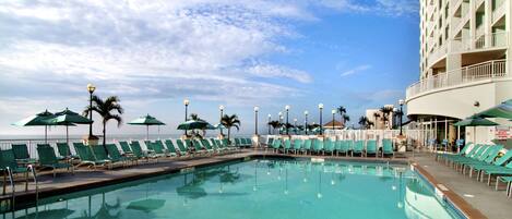 A pool area with lounge chairs and umbrellas, a clear sky, and a building in the background.