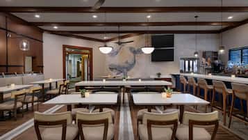 A restaurant with multiple tables and chairs, a mural of a whale, ceiling fans, and a bar area.