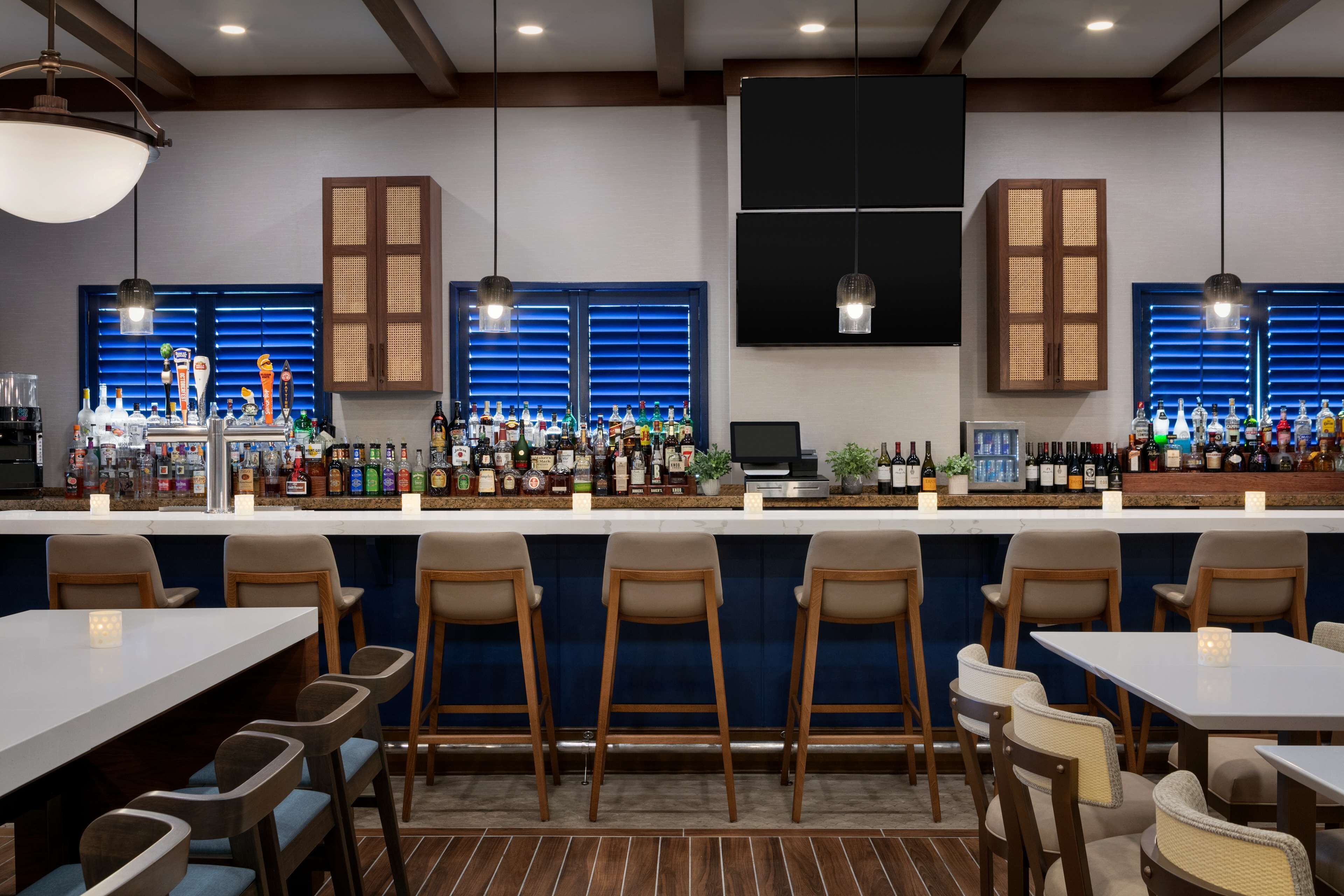 A bar area with multiple seating options, including bar stools and tables, and a variety of bottles and glasses on the counter.