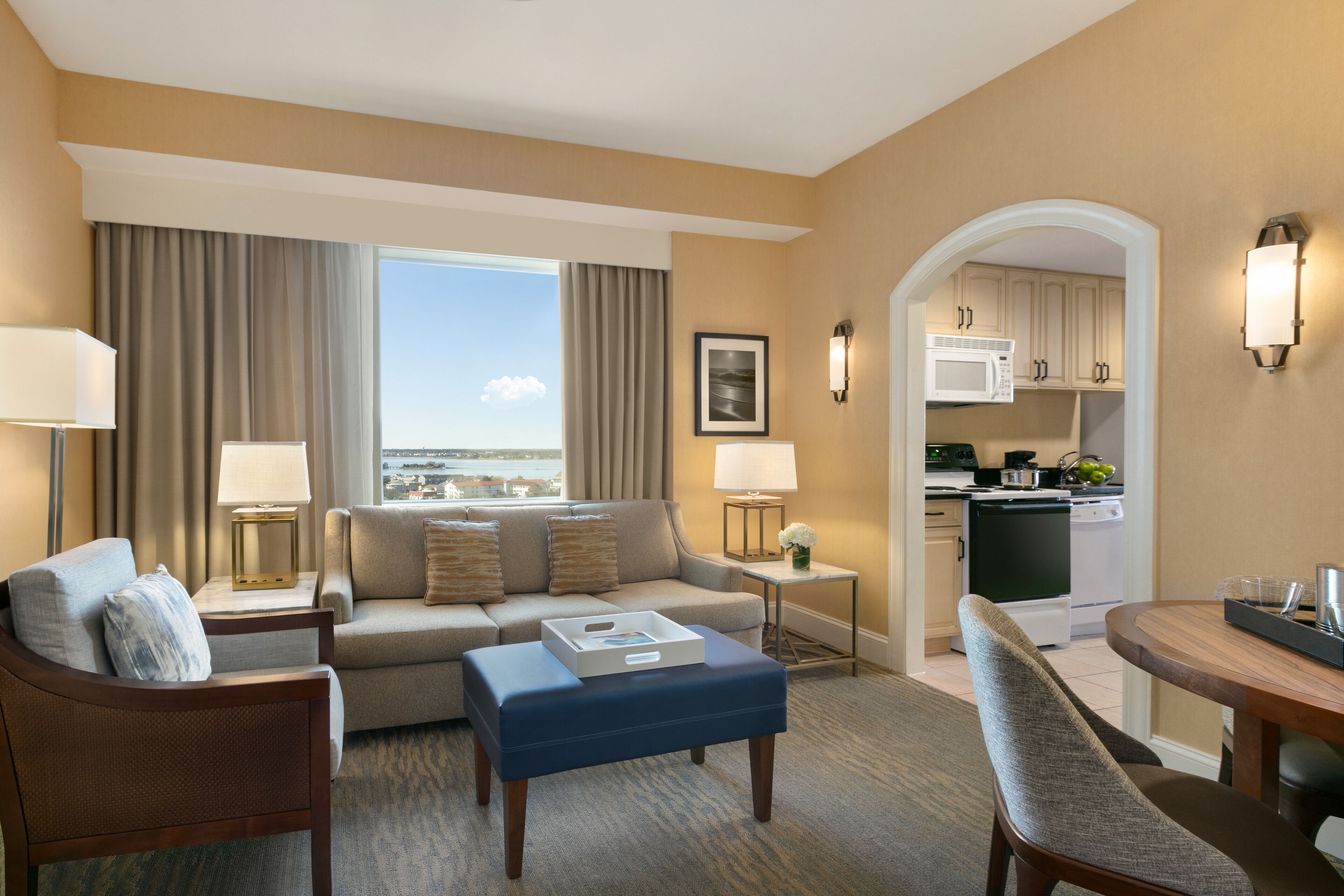 A hotel room with a living area, kitchenette, and a view of the city.