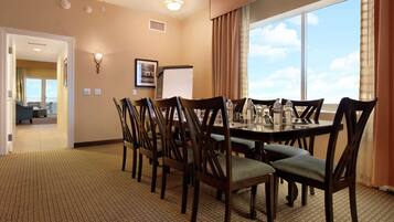 A conference room with a large table, chairs, a projector screen, and a view of the sky through a large window.