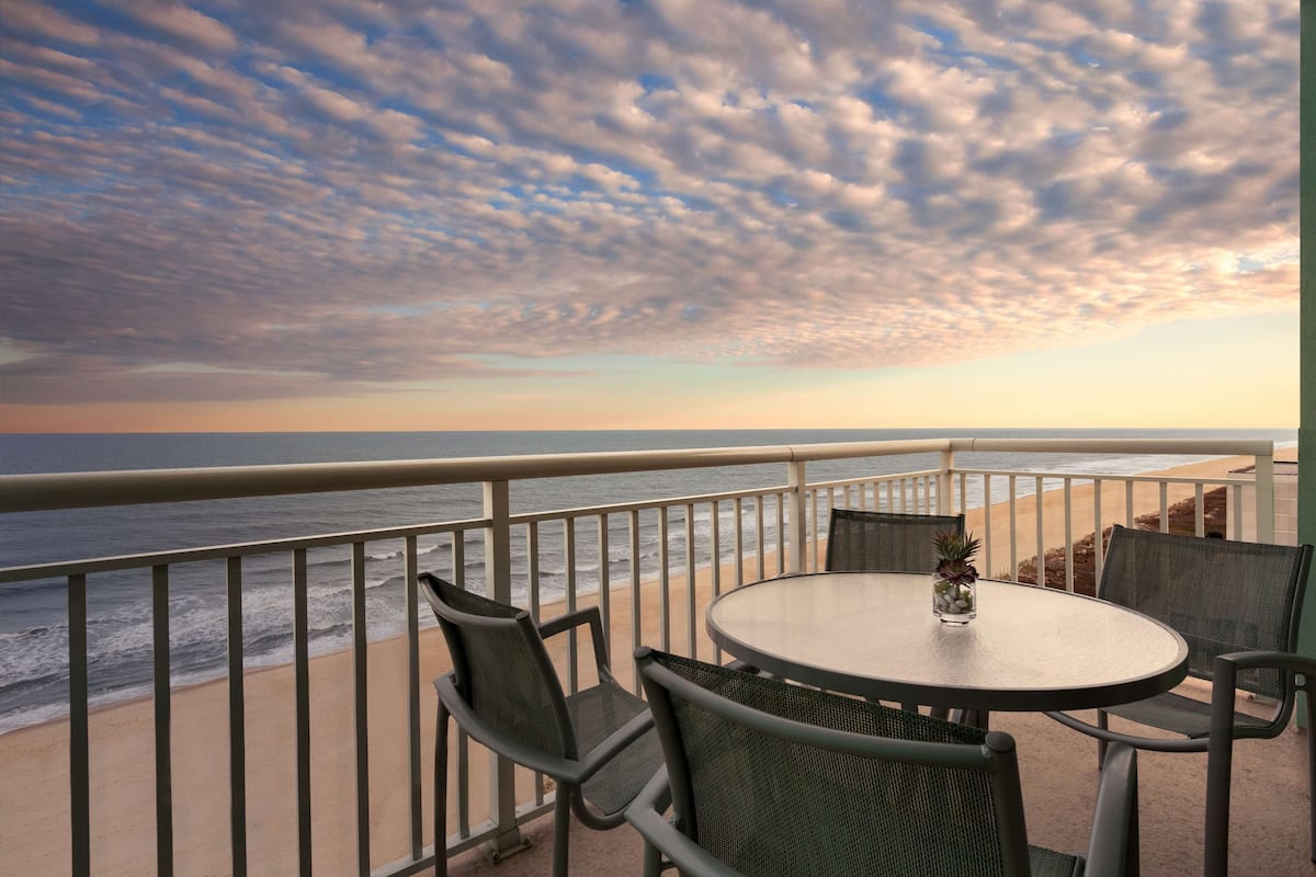 Un balcon avec une table ronde et des chaises, donnant sur la plage et l’océan.