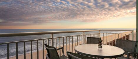 A balcony with a round table and chairs, overlooking the beach and ocean.