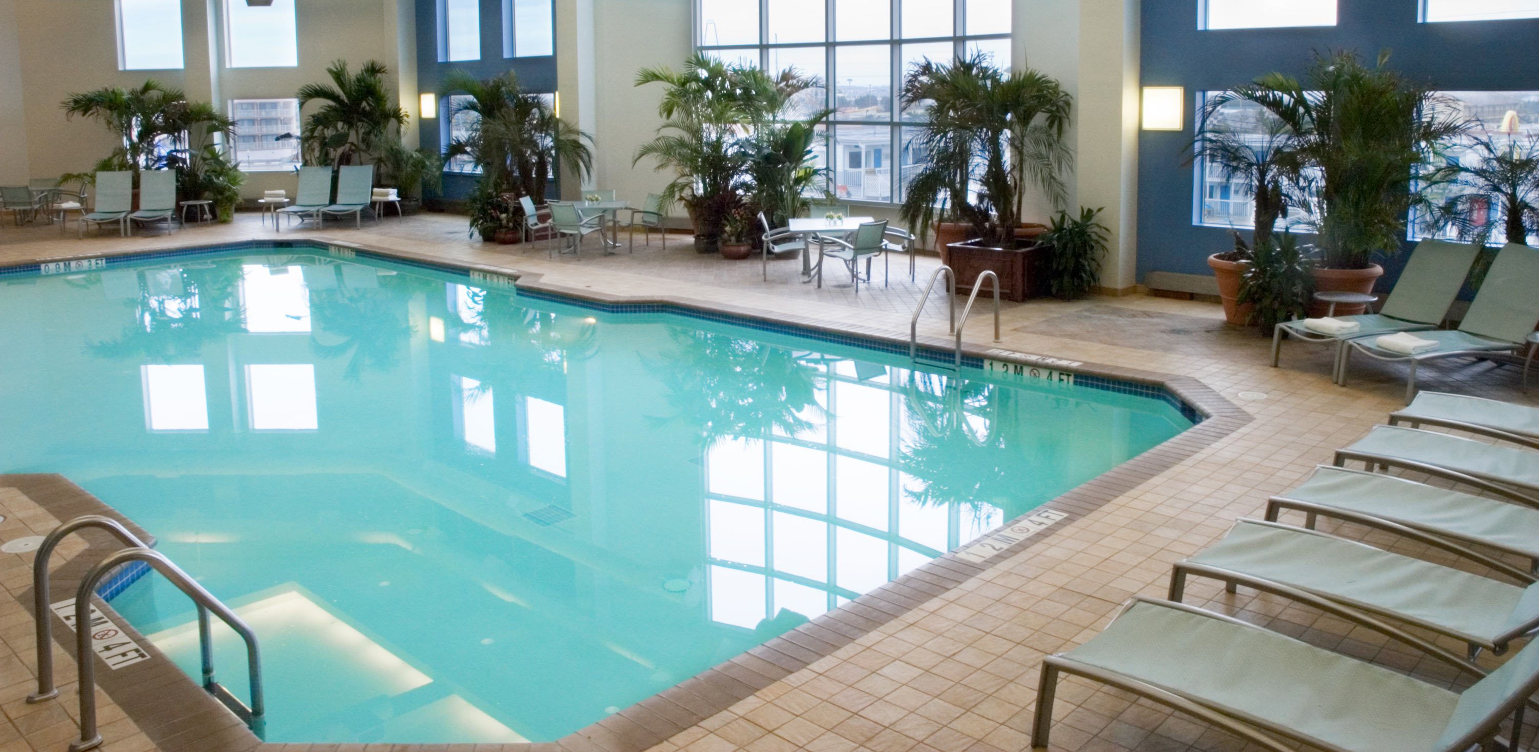 An indoor swimming pool with clear water, surrounded by lounge chairs and potted plants.