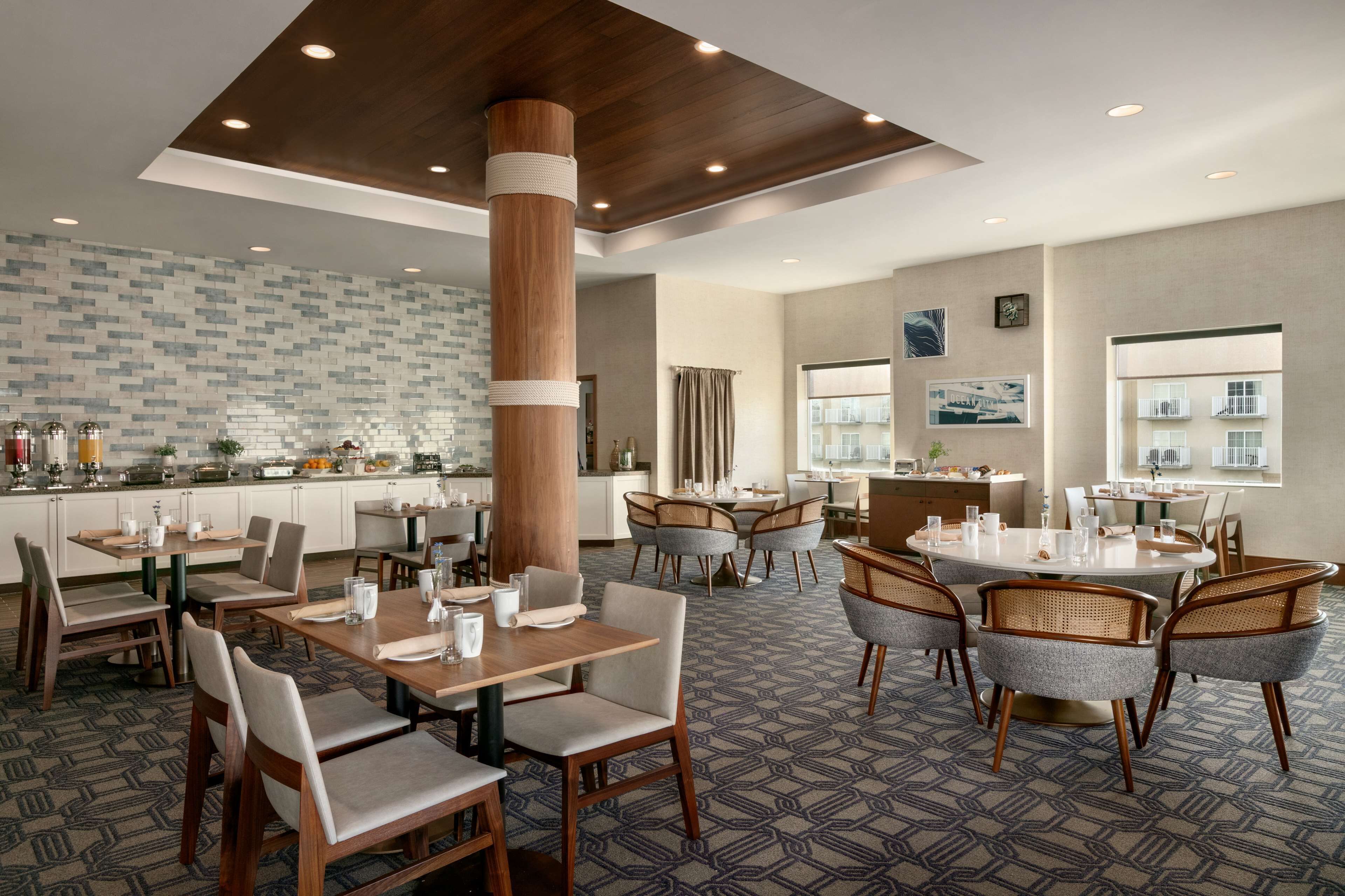 Un comedor de hotel con varias mesas y sillas, un pilar grande y una cocina al fondo.