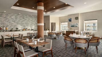 Un comedor de hotel con varias mesas y sillas, un pilar grande y una cocina al fondo.