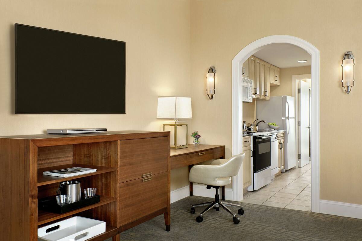 Une cuisine moderne avec des appareils électroménagers blancs, un bureau en bois avec une chaise et un grand téléviseur à écran plat fixé au mur.