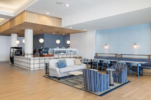 Un vestíbulo de hotel moderno con una zona de estar central, una kitchenette y una pared con estampado.