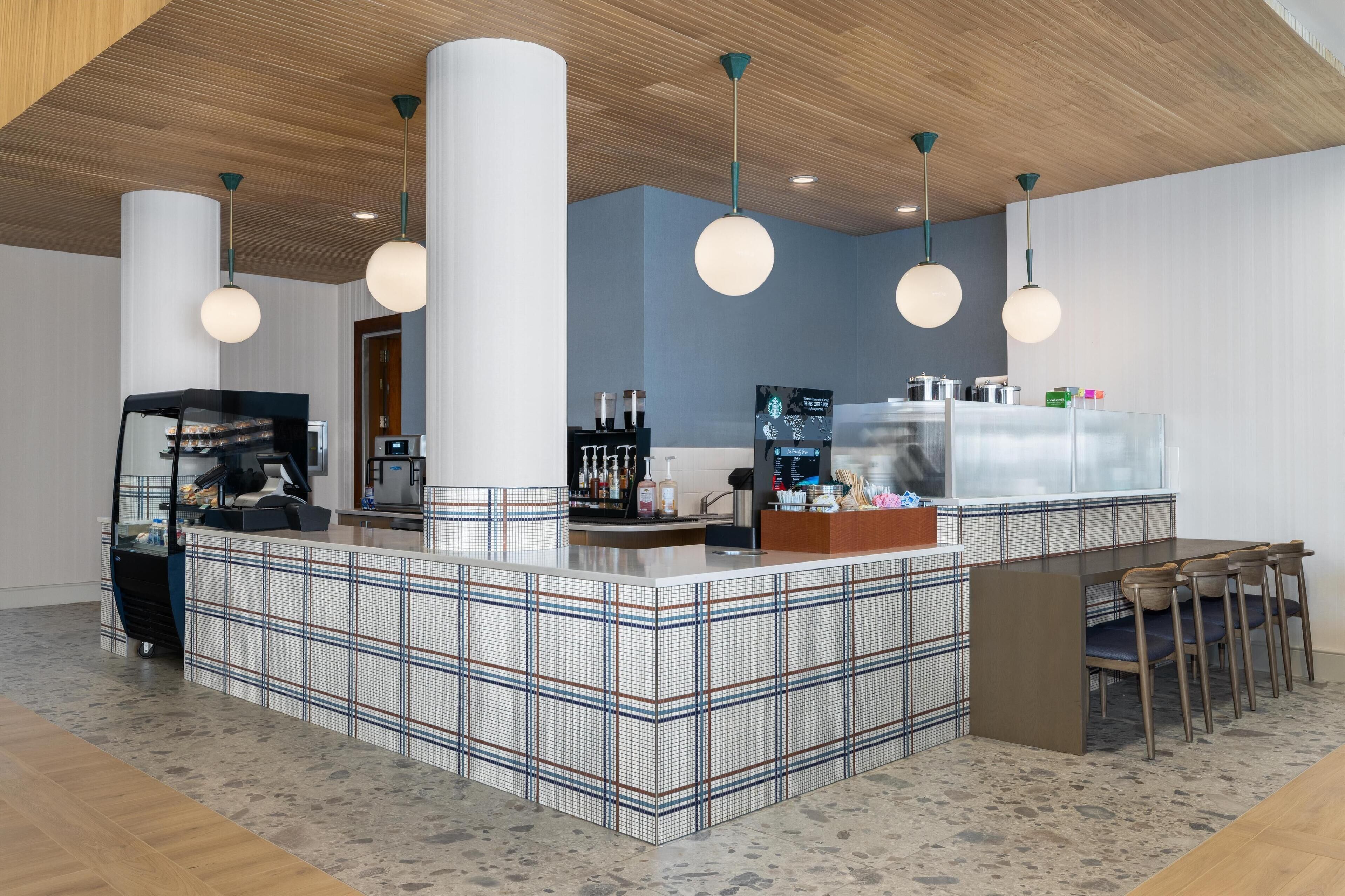 A modern bar area with a checkered floor, a counter with a coffee machine, and pendant lighting.