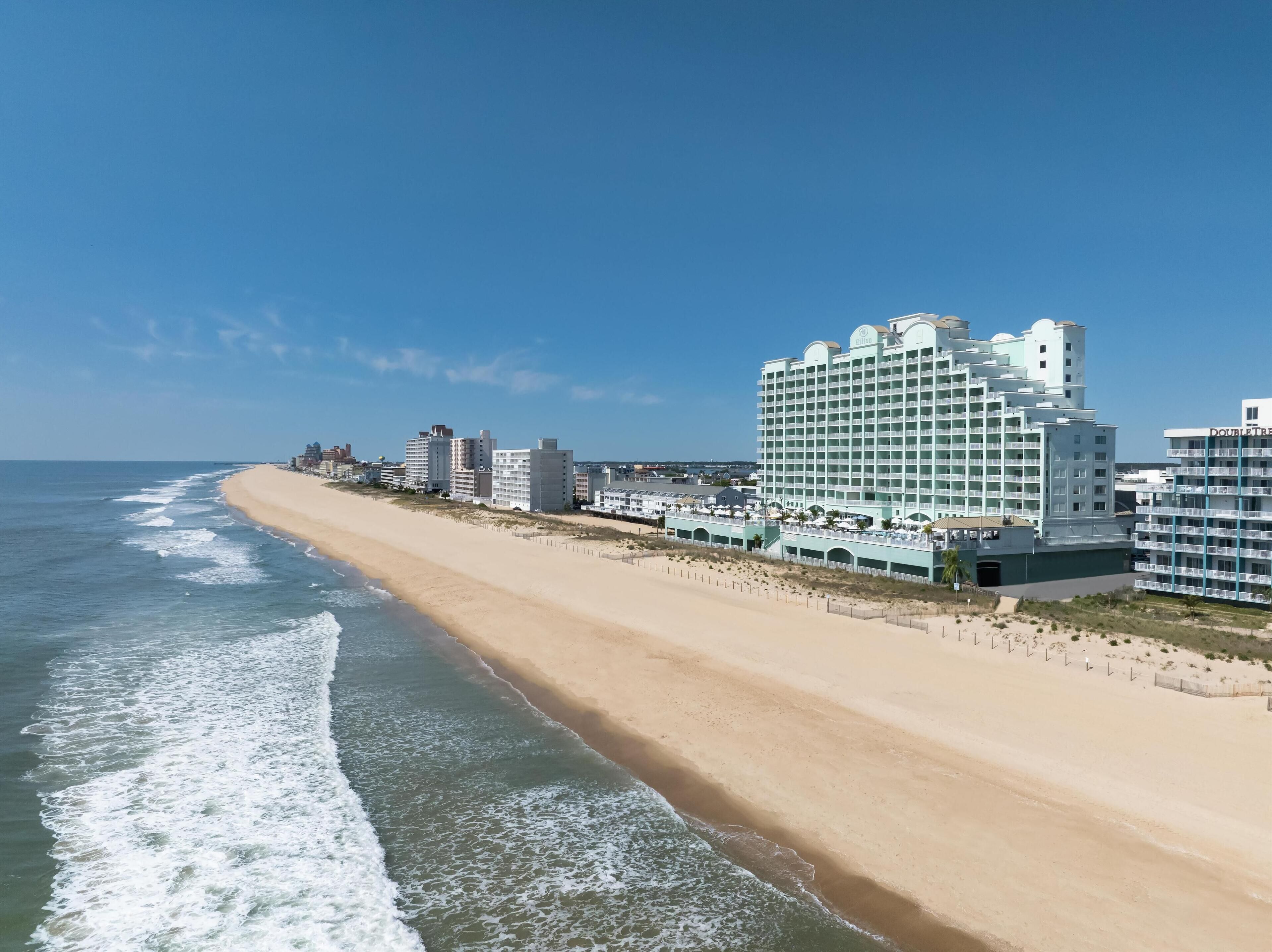A beachfront hotel with multiple floors, a sandy beach, and ocean waves.