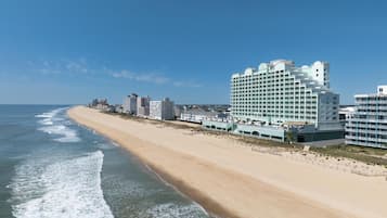 A beachfront hotel with multiple floors, a sandy beach, and ocean waves.